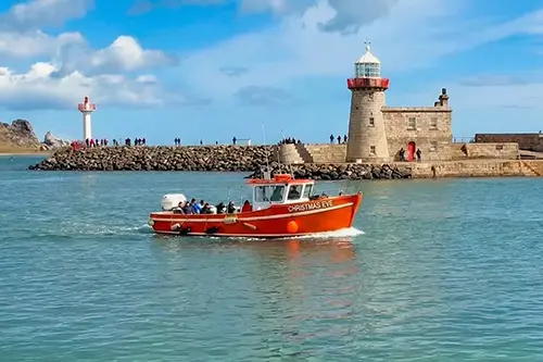 Ireland's Eye Ferry enters Howth Harbour, with pier and lighthouse in background.