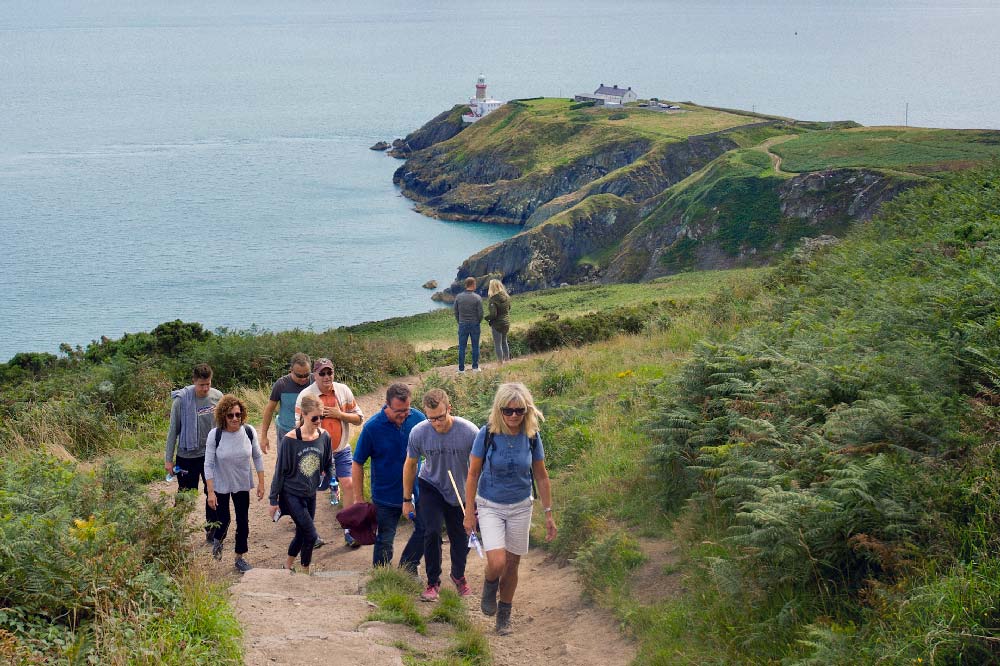 Group of walkers climbing the path at Howth Head. Lighthouse and coast in the background.