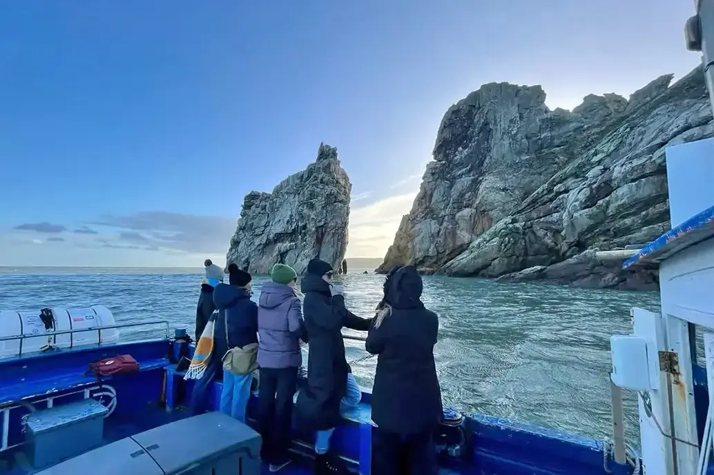 Five people view the rocky shoreline of Ireland's Eye from the Ferry.