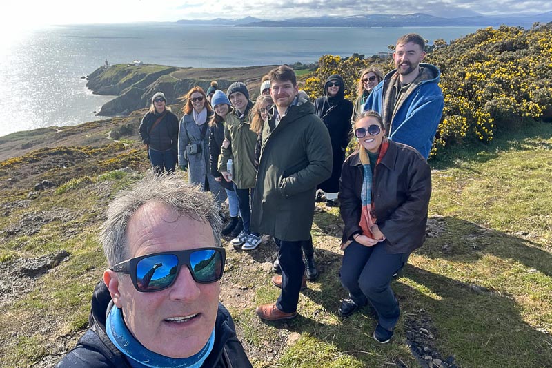 Tour guide and corporate group on Howth Head. Lighthouse and seascape in the background.