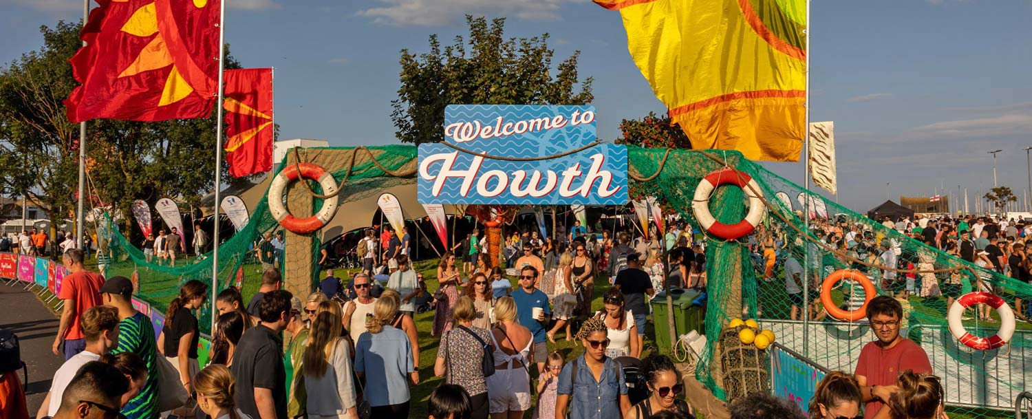 Crowd at the entrance to Howth Maritime Festival with flags flying above.