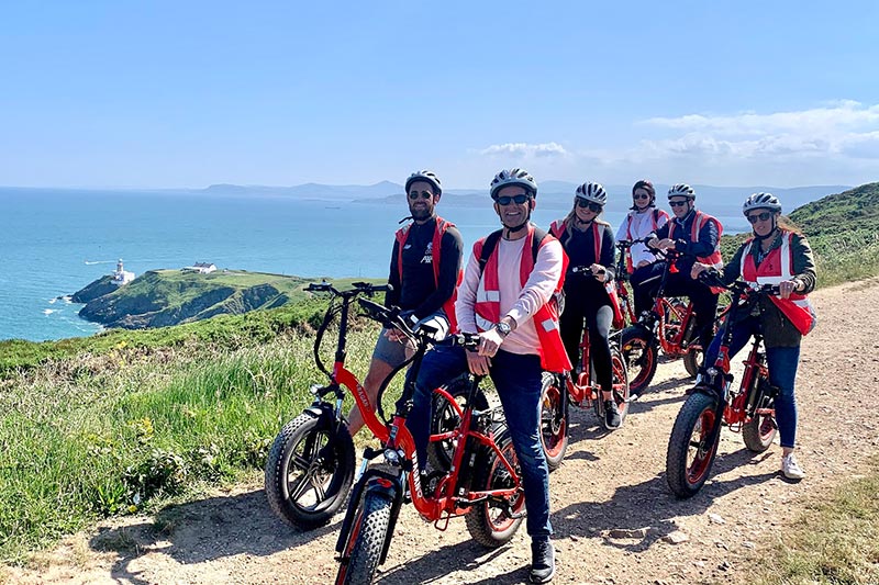 Bike Tour Group on top of Howth head with lighthouse visible.