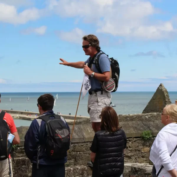 Howth Adventures Tour Guide standing on a ledge points over the wall and speaks to the tour group.