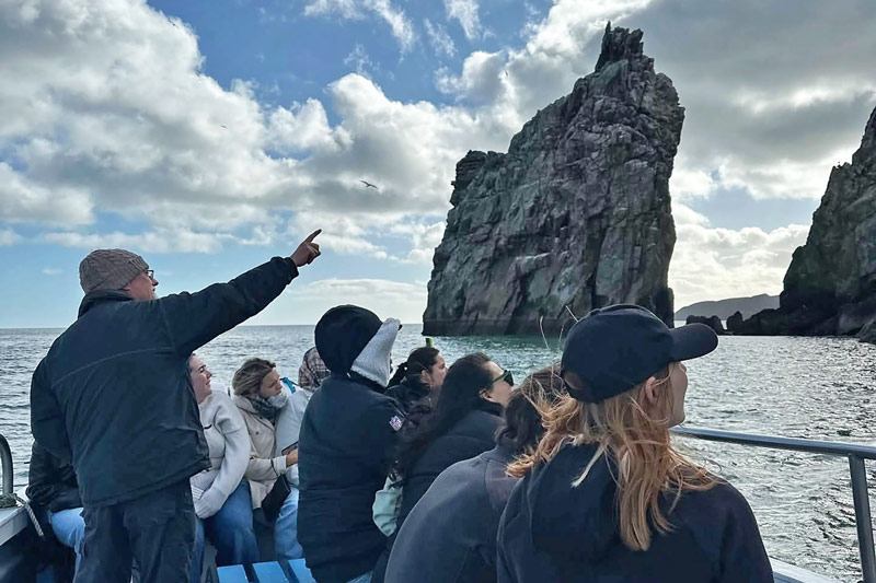 Ireland's Eye Ferry Tour Guide points at the cliff edge to the group.