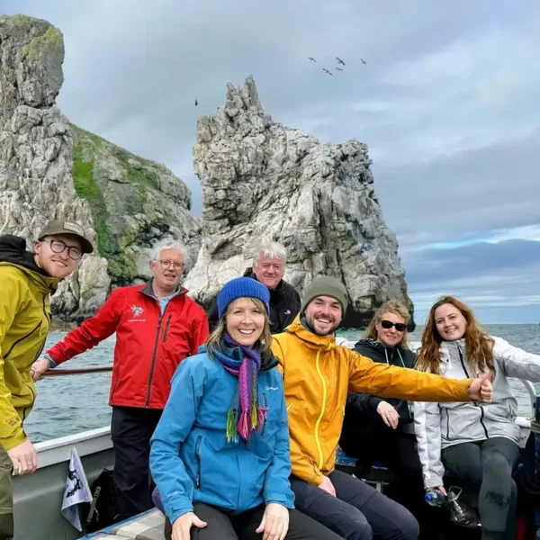 Irelands Eye Ferry boat tour group pose on-board, in front of island sea stacks.