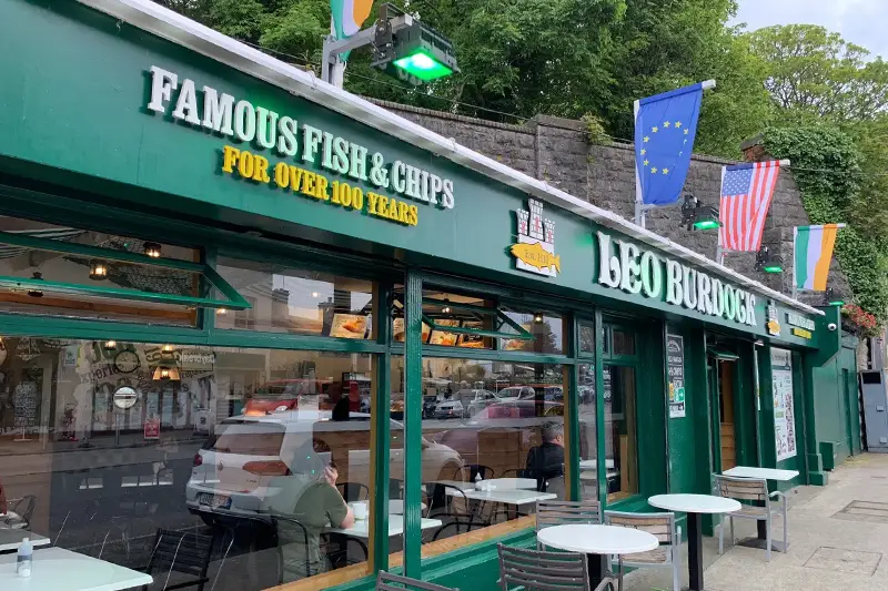 Green shopfront of Leo Burdocks, fish and chips shop in Howth, with tables and chairs outside.