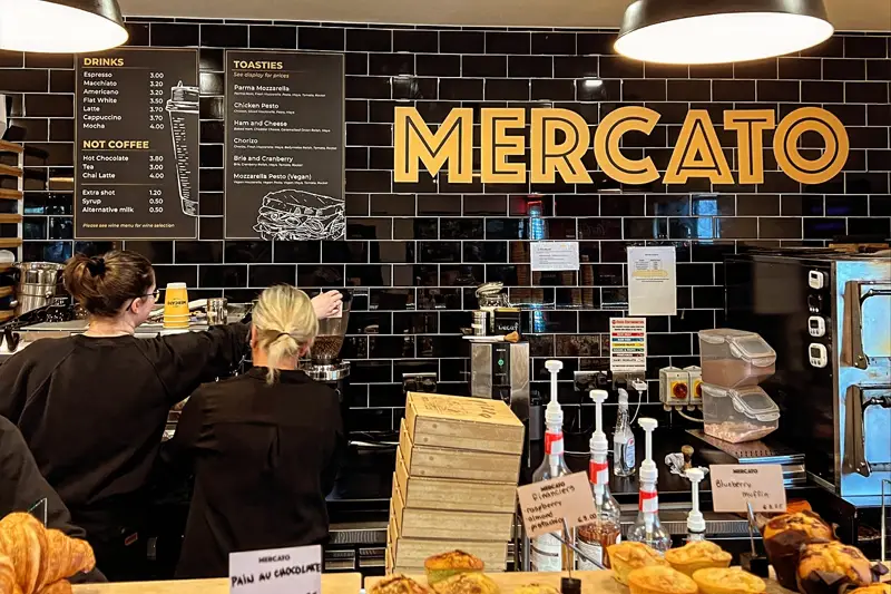 View of staff at work in Mercato, Howth with black wall tiles and large MERCATO signage.
