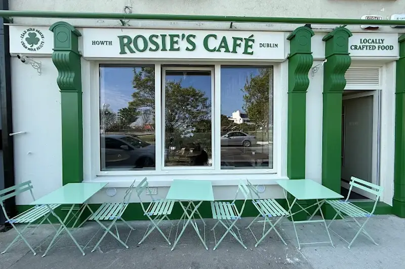 Green and white shopfront of Rosie's Café in Howth, with tables and chairs outside.