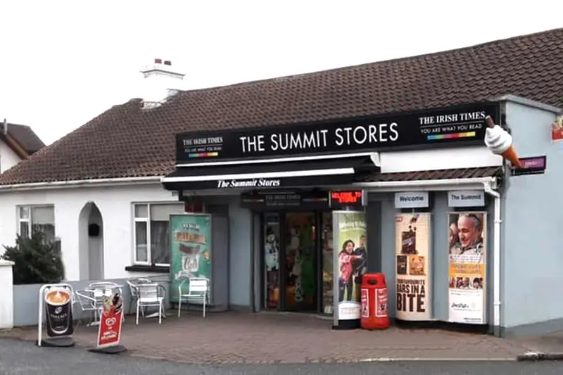 Shopfront of 'The Summit Stores' in Howth, with black sign, white lettering and tables and chairs outside.