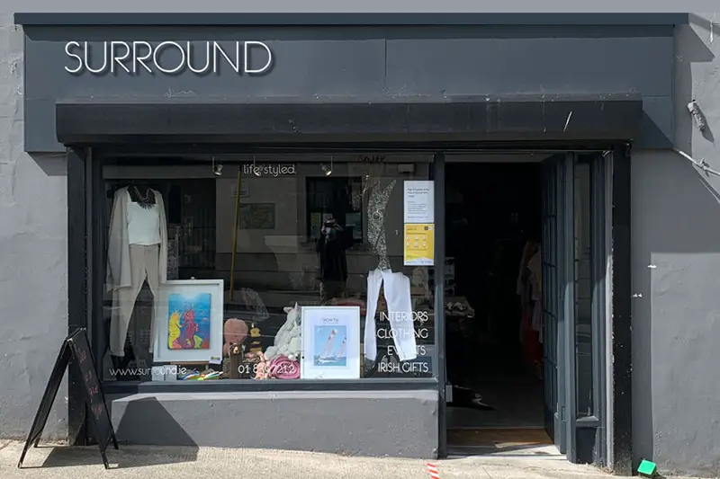Shopfront of 'Surround' in Howth, with gray sign, white lettering and sandwich board sign outside.