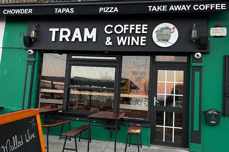 Shopfront of 'Tram Coffee & Wine' in Howth, with green wall, black and white signage and tables and chairs outside.
